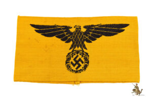 This is a textbook original, Yellow State Service Armband - Reichsdienst Ärmelband, in near mint condition. It’s Bevo, machine woven construction, as most of these were. The body of the armband is made from a fairly sturdy yellow cotton, with strong original color. A large and impressive German national eagle and swastika emblem is woven in black thread on the front. The upper and lower edges show the expected woven edging. The short edges on the reverse have been factory machine sewn together with yellow thread. Inside, the eagle and swastika emblem is visible in reverse, a characteristic result of the machine weaving process used to make these. There are no holes or tears to the fabric or to the woven design, but the armband does show some minor spotting as shown. This State Service armband shows only very slight age. Overall, it’s a great representative example of this popular armband style. The condition of this Yellow State Service Armband - Reichsdienst Ärmelband is near mint condition.